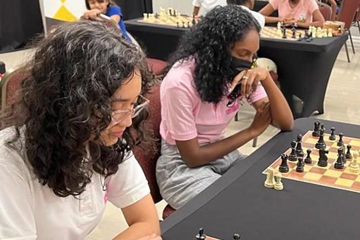 Women and girls seated at boards during a chess event.